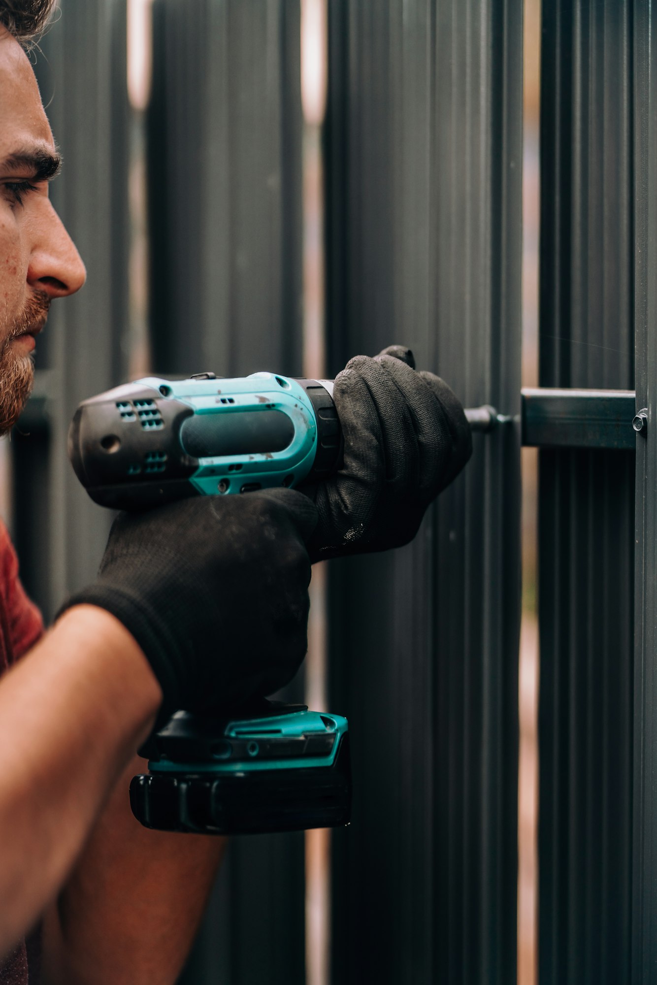 Worker using screwdriver drilling and screwing metal screws into metal fence
